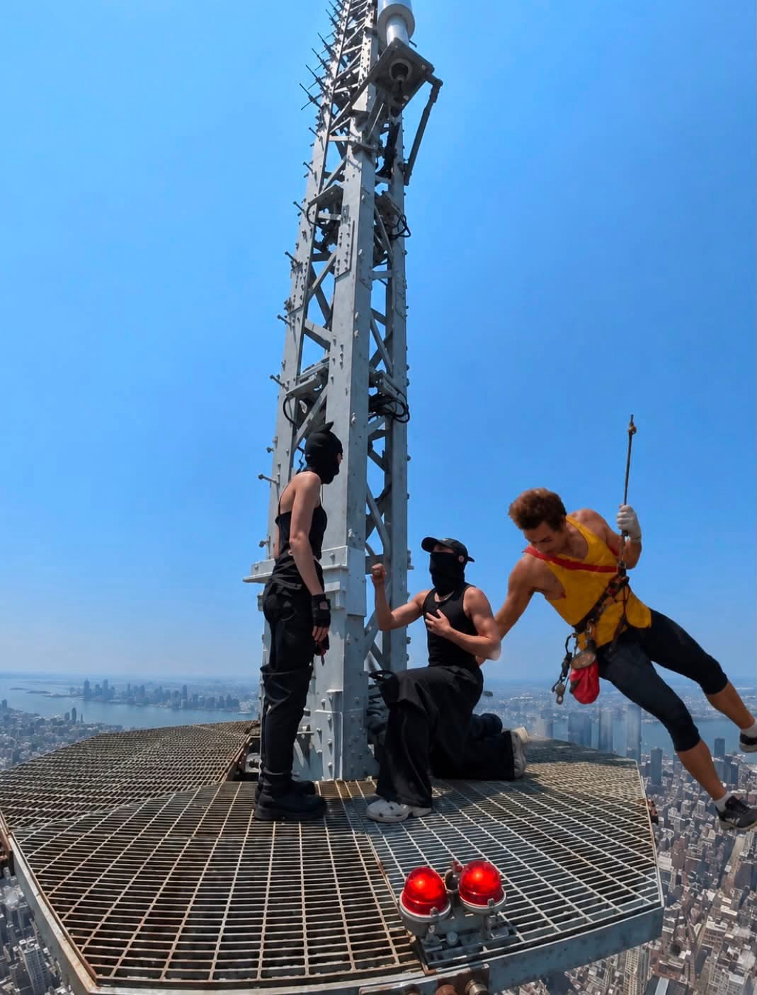 Kramer from seinfwld dangles from a rope next to te couple that famously cimbed the empire state building.