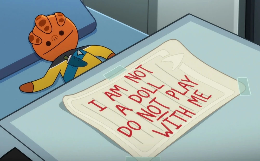 Kayshon from Star Trek: Lower Decks, having been turned into a puppet. There is a sign next to him that says, "I am not a doll do not play with me"